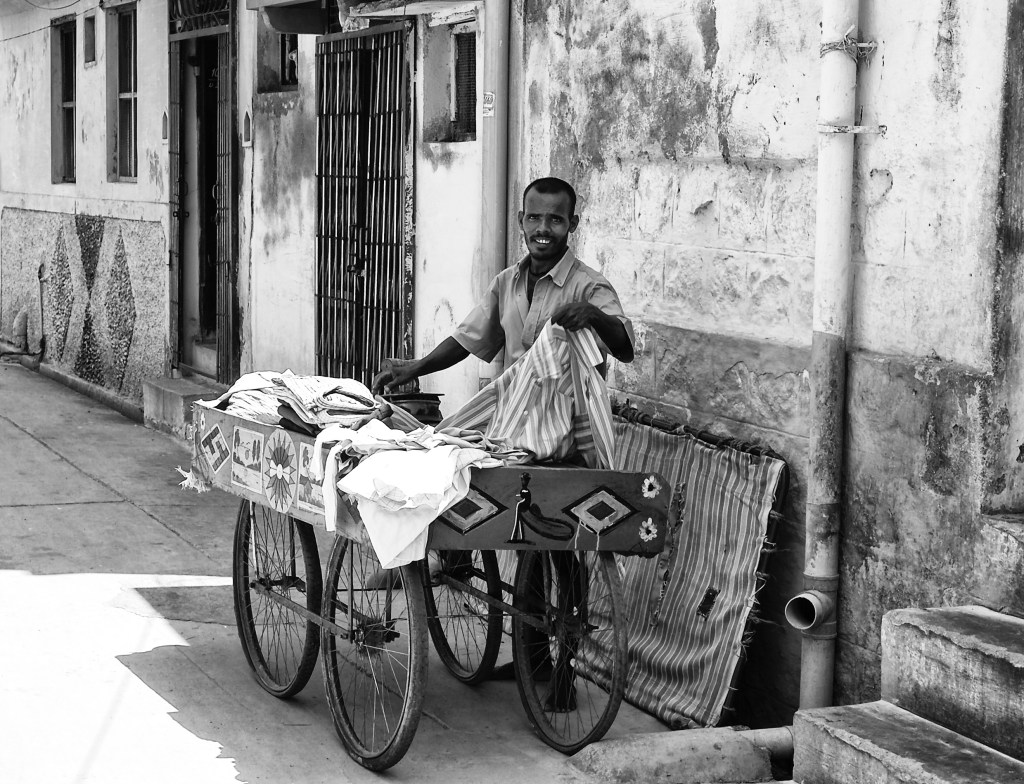 Iron(ing) man on his work, out in the streets with his push cart. The ironing is heated up by charcoals inside. Virudhunagar, India.