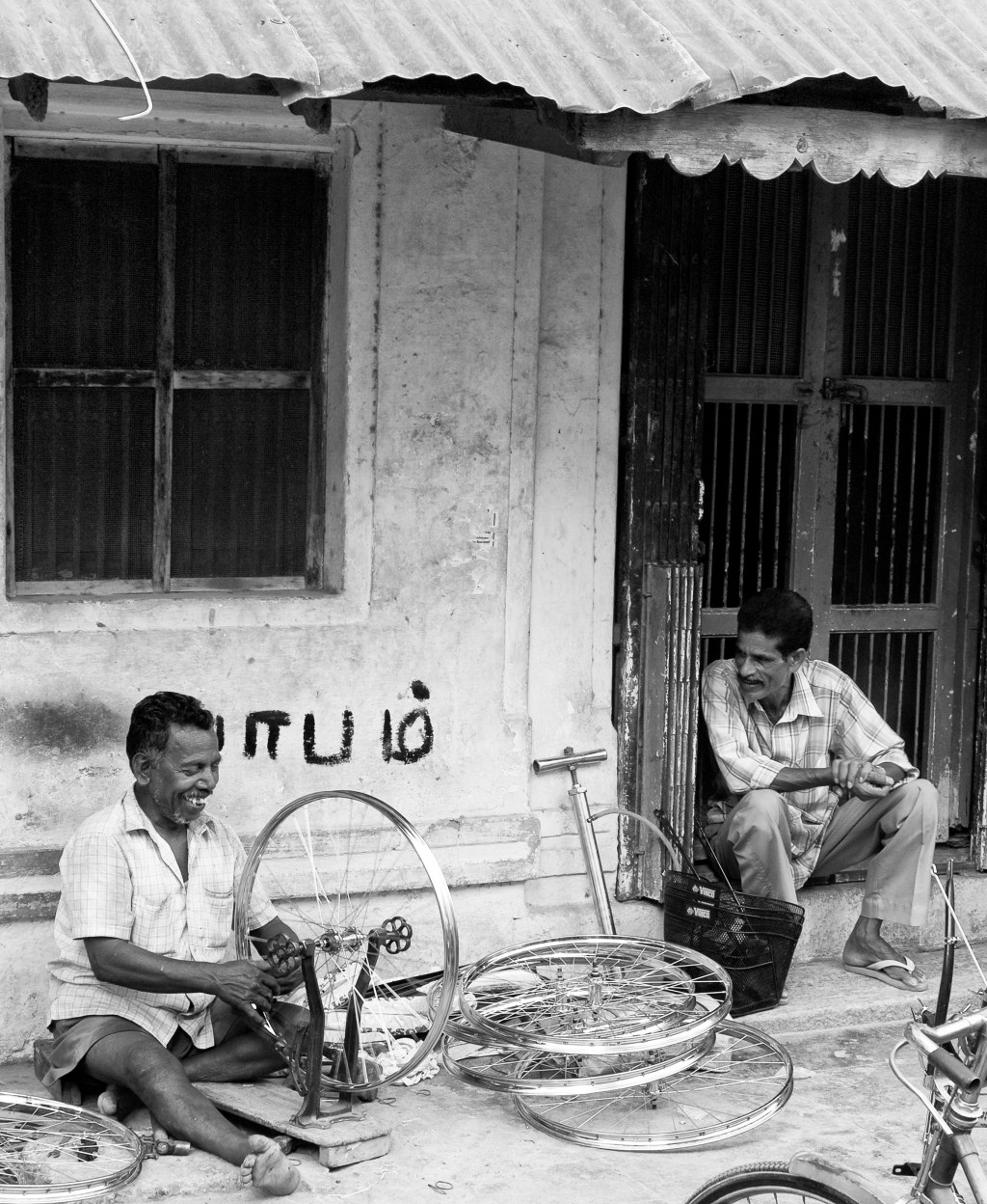 A bicycle mechanic straightening and aligning the wheel rims and spokes. Madurai, India