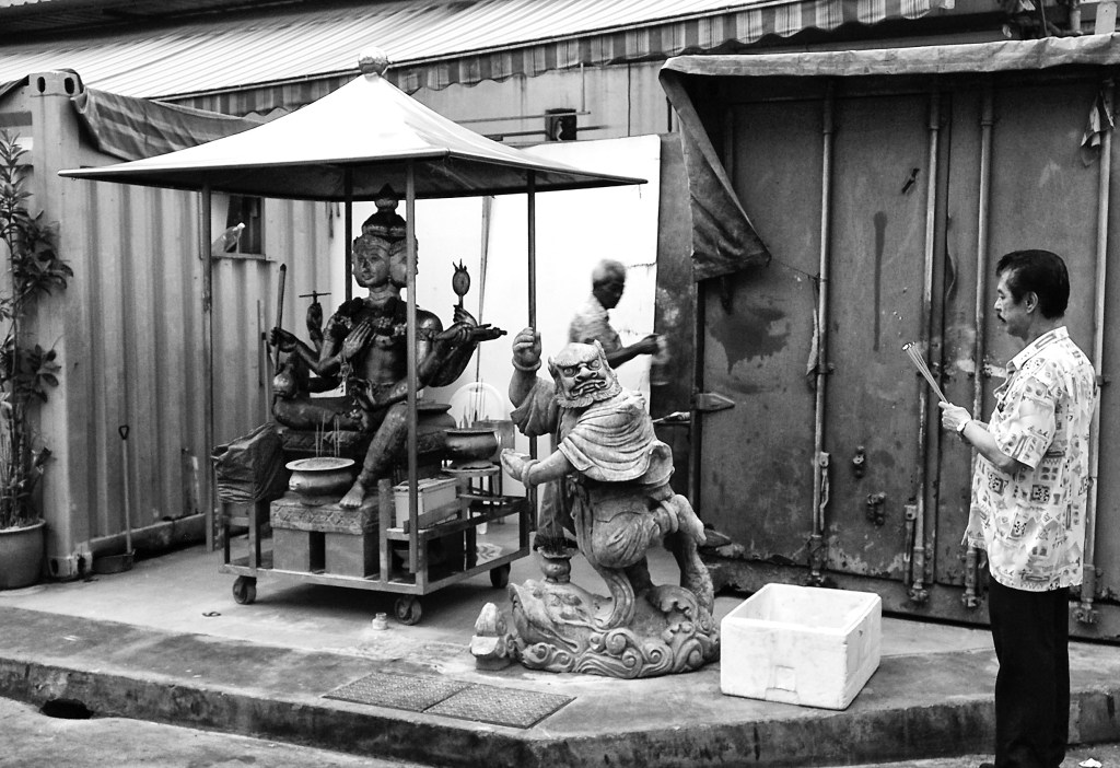 A worshipper offering incense sticks to the four-faced Brahma (Phra Phrom) God, beside with another demigod, at a makeshift temple by a lane side. Bugis Street, Singapore