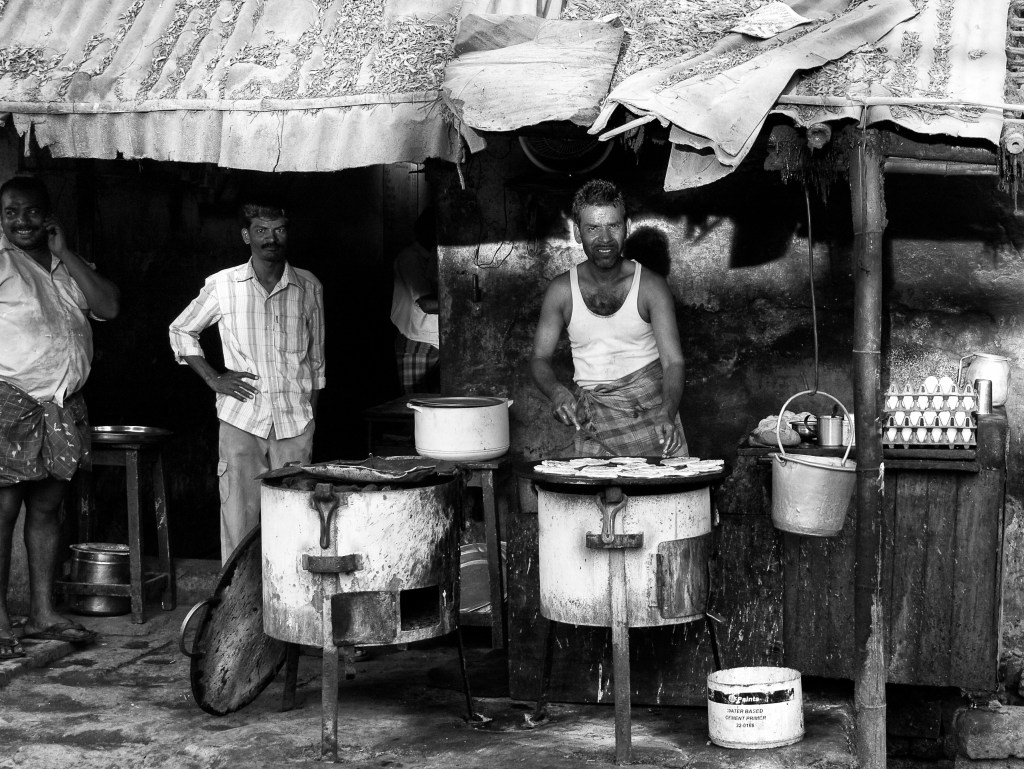 A cook frying parottas in the charcoal stove at a roadside food-stall. Virudhunagar, India.