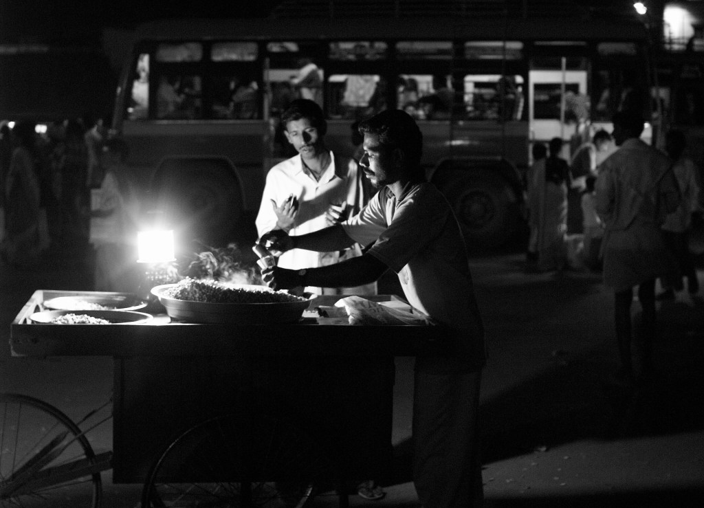 A street vendor selling boiled peanuts in his push cart setup, lightened up by the petromax lantern. Virudhunagar, India.