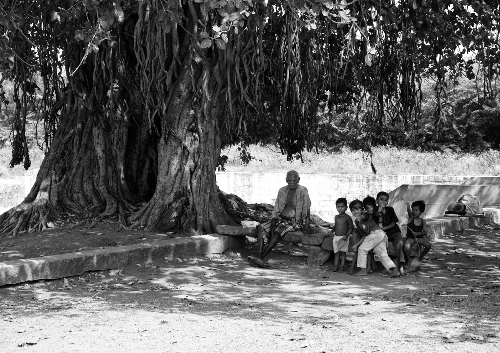 Old men rest while kids play, under a banyan tree. Chinna Vallikulam, Virudhunagar, India